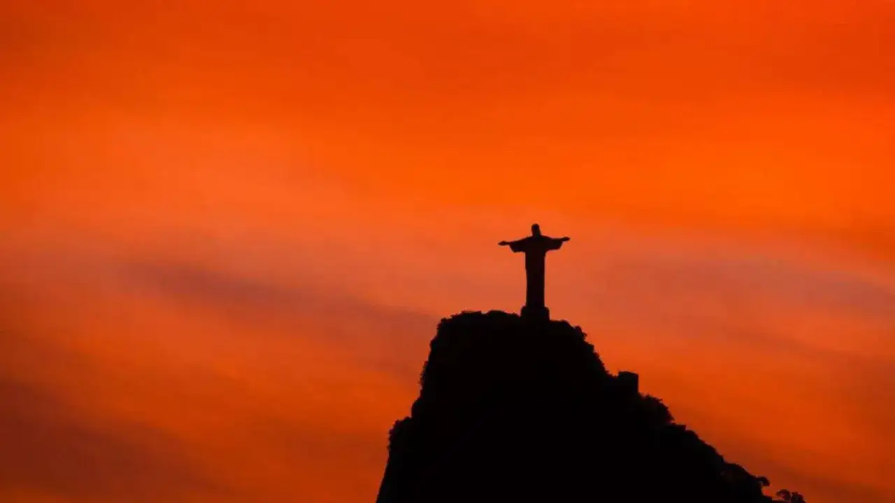 Die berühmte Christusstatue in Rio de Janeiro ragt silhouettenhaft vor einem leuchtend orangen Himmel auf.