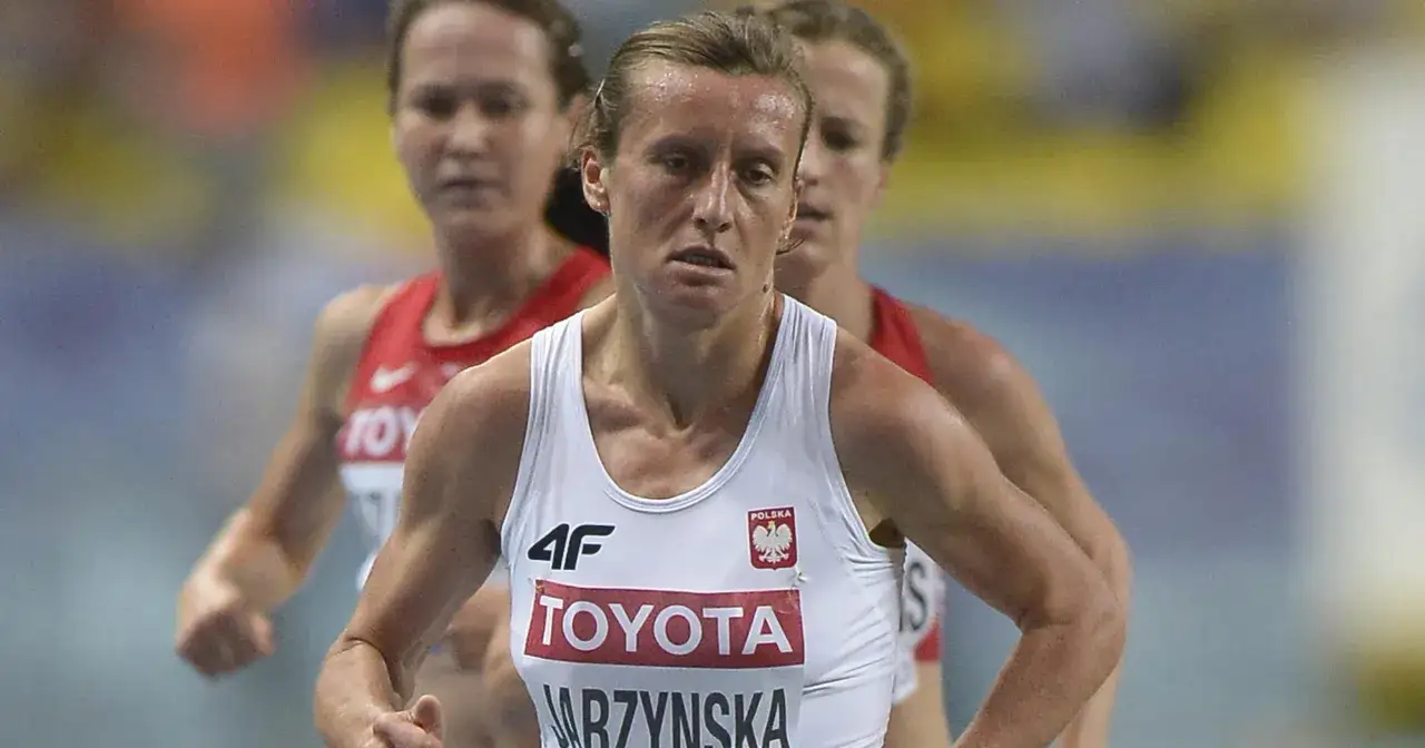 Karolina Nadołska w białej koszulce z logo Toyoty i godłem Polski biegnie podczas zawodów.