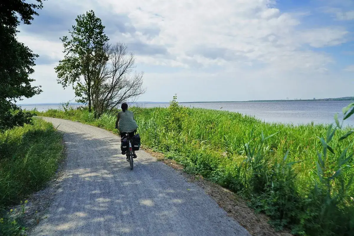 Osoba na rowerze z bagażem jedzie po płaskiej trasie rowerowej wzdłuż jeziora.