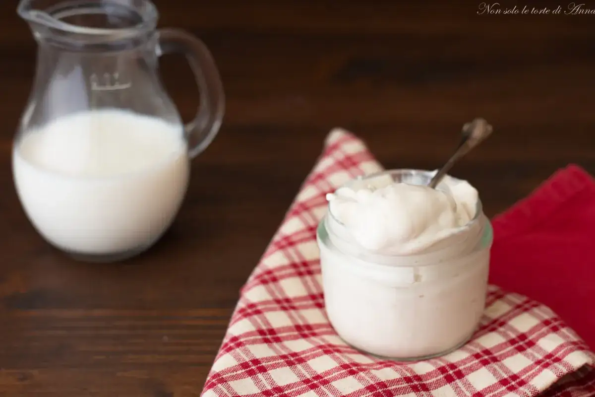 Un vasetto di cremoso yogurt greco fatto in casa, pronto per essere gustato, con una brocca di latte sullo sfondo.