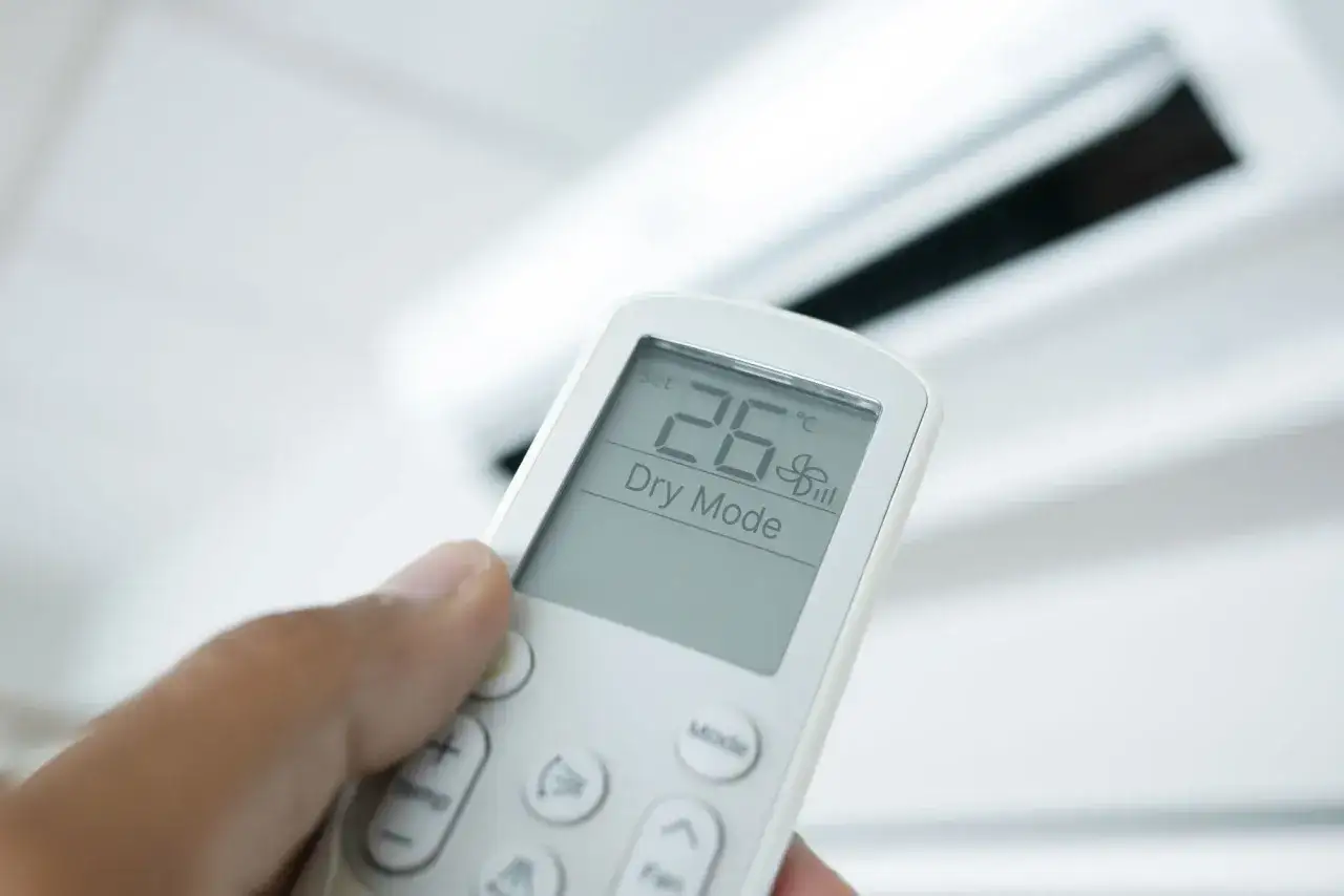 Une main tient une t&eacute;l&eacute;commande de climatiseur r&eacute;gl&eacute;e sur le mode 