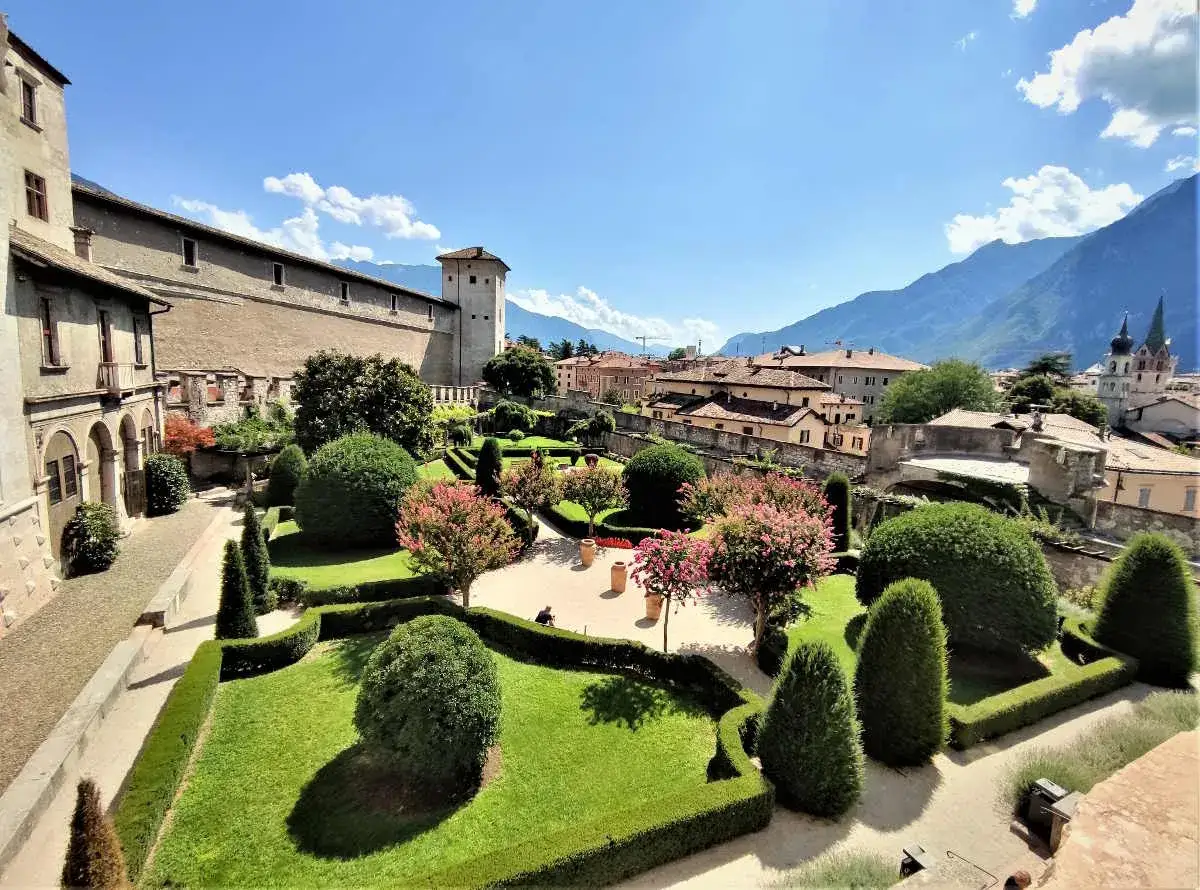 Giardino del **Castello del Buonconsiglio**, dove la **leggenda** narra di antichi segreti tra siepi curate e fiori rosa.