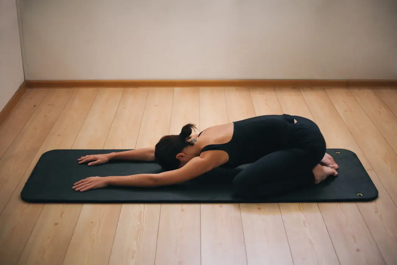 Frau in schwarzer Kleidung in der Kindeshaltung während einer Yoga-Periode.