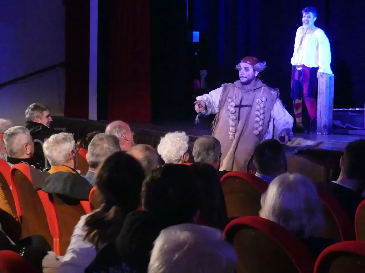 Attori in costume sul palco, il pubblico in platea rompe la **quarta parete teatro**.