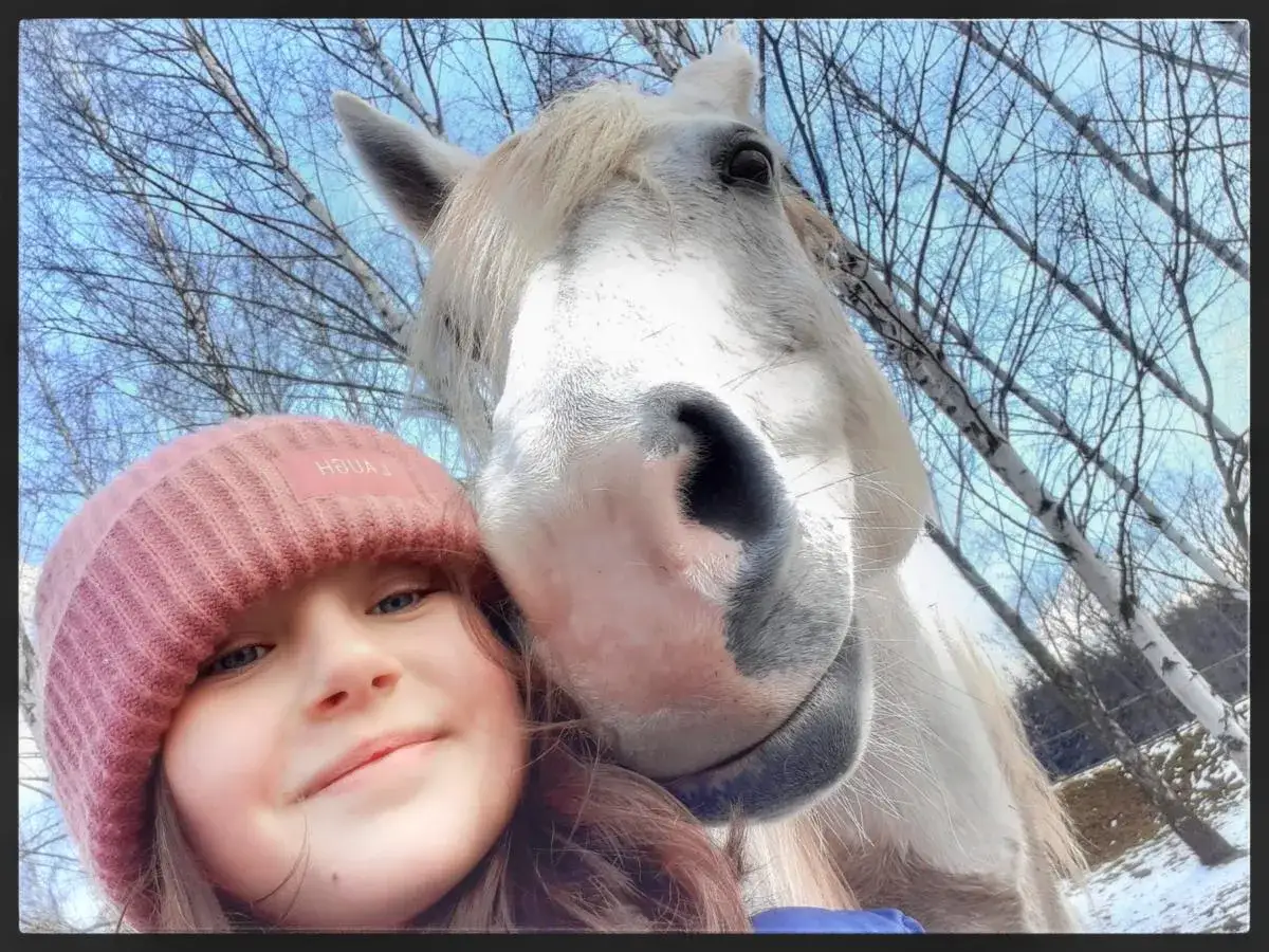 Dziewczynka w różowej czapce robi selfie z koniem. Idealne zdjęcie do konkursów fotograficznych dla dzieci.