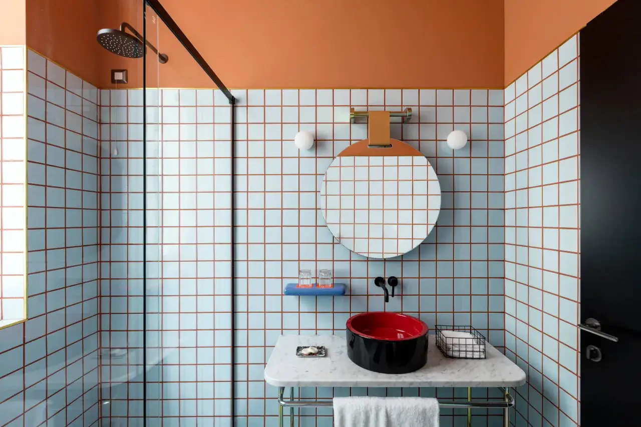 Bagno moderno con piastrelle azzurre e fughe color rame. Un lavabo nero e rosso spicca sul piano in marmo. Ideale per chi cerca consigli su come riempire le fughe delle piastrelle.