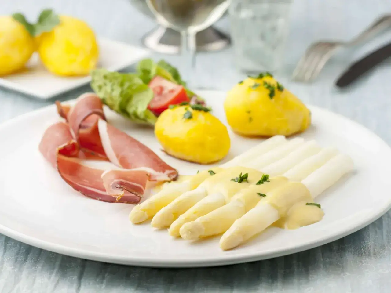 Spargel mit beurre blanc, Salzkartoffeln und Schinken auf einem Teller.