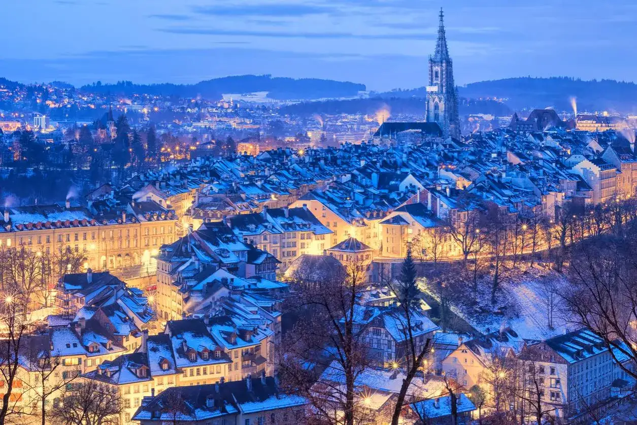 Suggestivi **posti da visitare in inverno Italia**: un panorama urbano innevato con un'imponente torre campanaria, luci calde che illuminano le case.