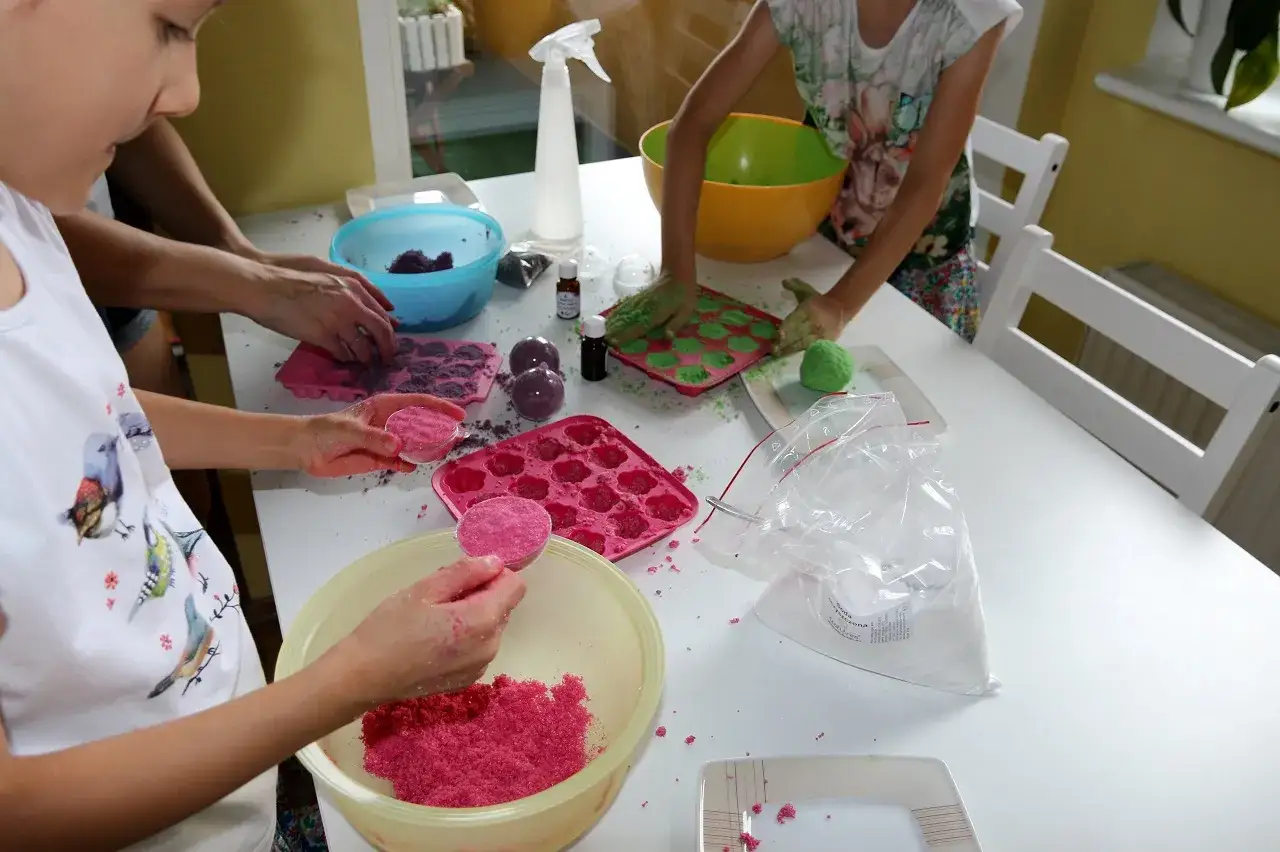 Dzieci tworzą kule do kąpieli diy, wsypując kolorowy proszek do foremek.