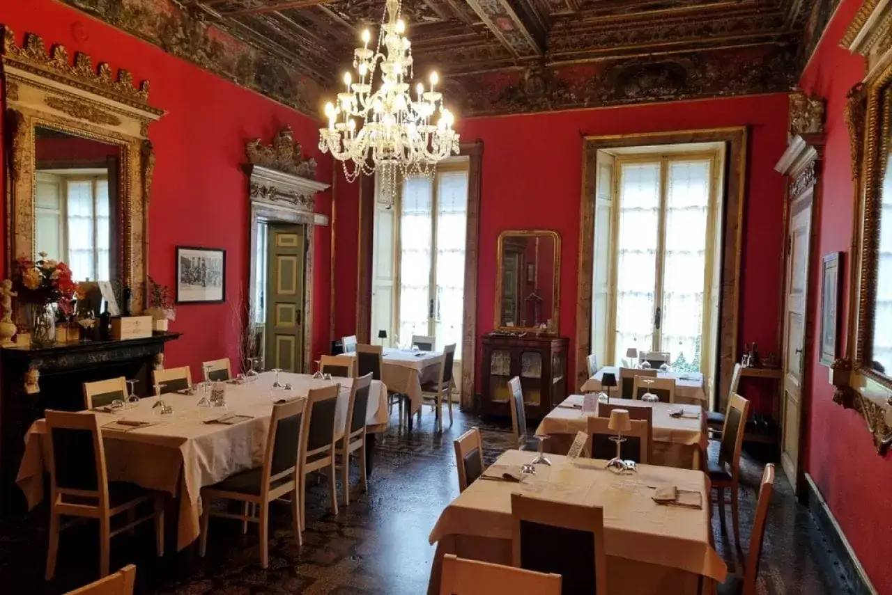 Sala elegante con tavoli apparecchiati, ideale per scoprire dove mangiare a Cremona. Lampadario imponente e pareti rosse creano un'atmosfera raffinata.