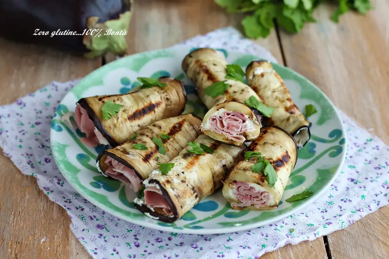 Involtini di melanzane grigliate ripieni di formaggio e prosciutto, guarniti con prezzemolo fresco.