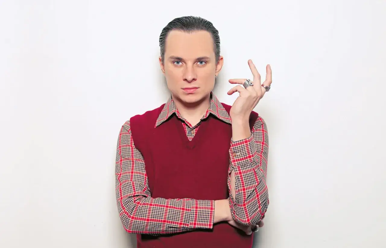 Ralph Kaminski, artysta o charakterystycznym stylu, w bordowym sweterku i koszuli w kratę. Jego wzrost jest tematem dyskusji.