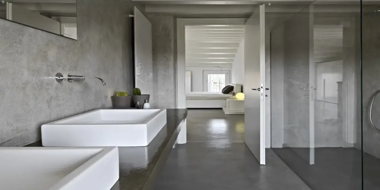 Salle de bain moderne avec murs et sol en résine grise, lavabos blancs et douche vitrée.