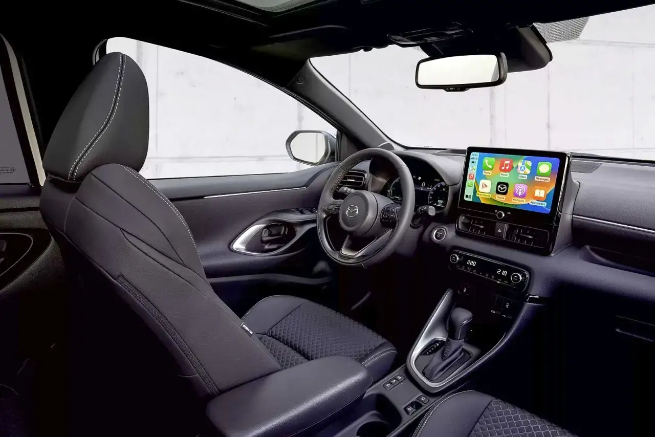 Wnętrze mazda 2 hybrid: skórzane fotele, nowoczesny ekran multimedialny z ikonami aplikacji i kierownica.