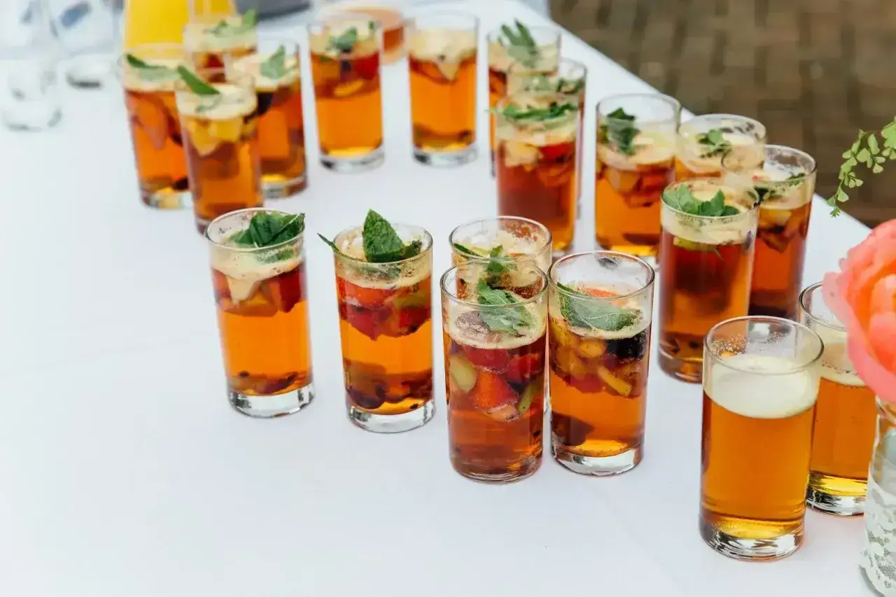 Orzeźwiające drinki na wesele przepisy: szklanki z bursztynowym napojem, owocami i miętą. Idealne na letnie przyjęcie.