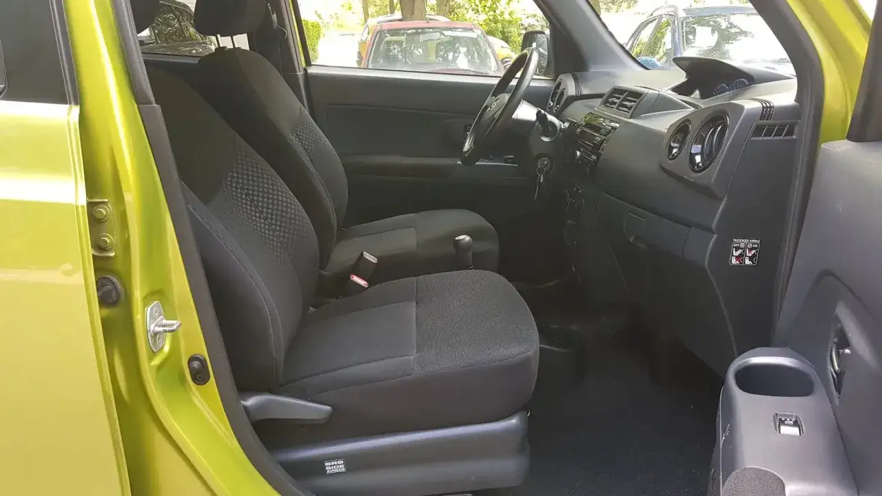 Wnętrze Daihatsu Materia: czarne fotele, deska rozdzielcza z radiem i nawiewami, widoczna dźwignia zmiany biegów.