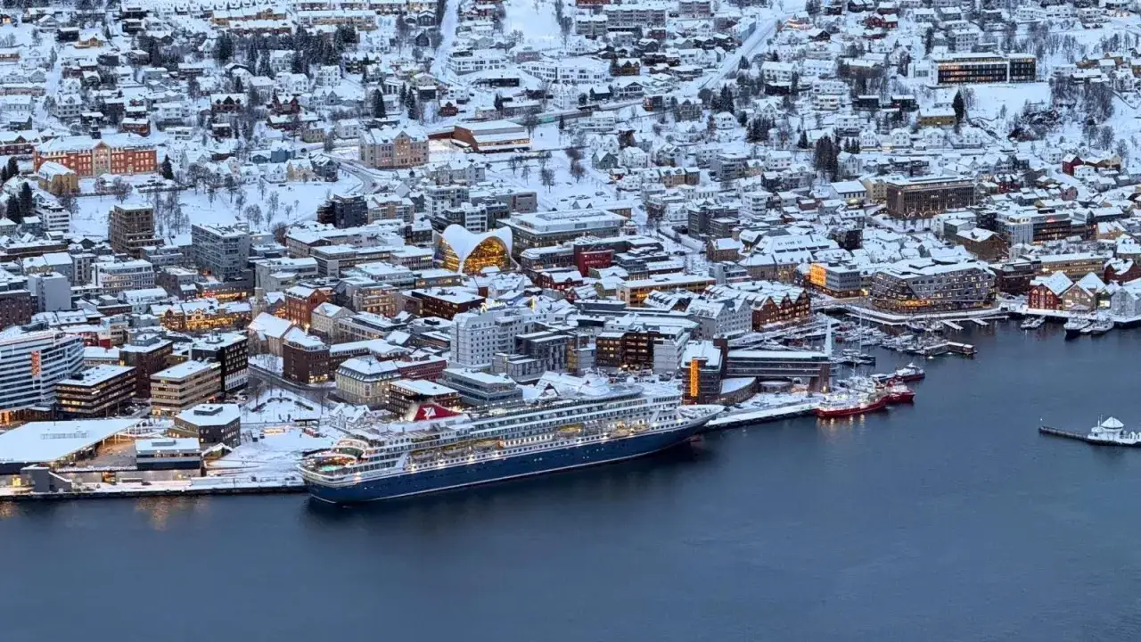 Schneebedeckte Stadt und ein großes Kreuzfahrtschiff im Tromsø Hafen.
