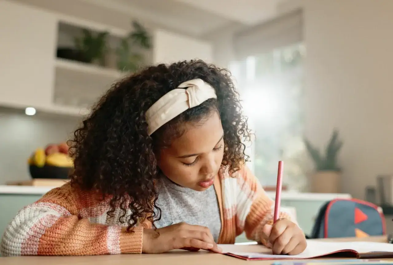 Niña concentrada en su dictado de 2 primaria, escribiendo con un lápiz rosa.