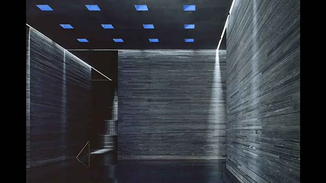 Intérieur des thermes de Vals Zumthor, avec murs en pierre sombre, éclairage zénithal bleu et jeux de lumière.