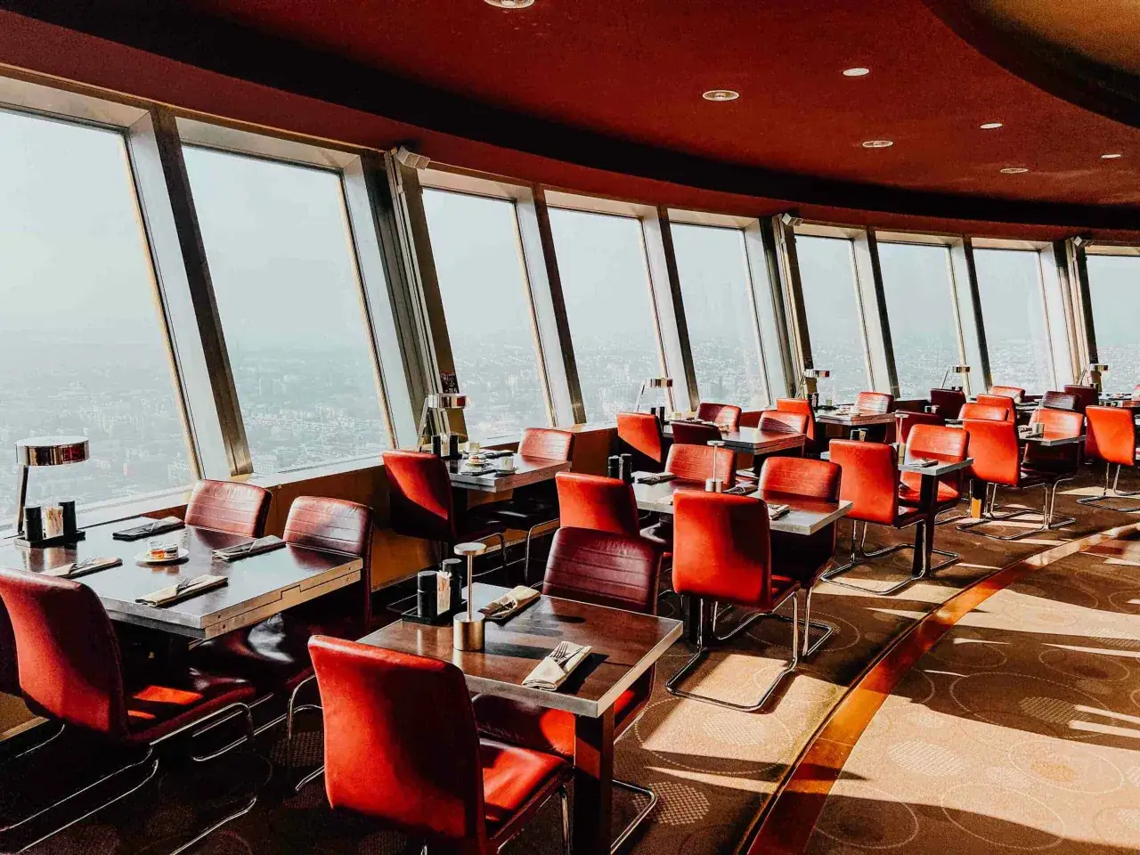 Rote Ledersitze und Tische in einem Restaurant mit Panoramablick auf die Stadt, das an den Alexanderplatz erinnert.