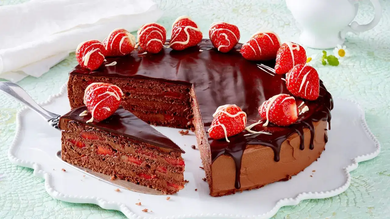 Eine k&ouml;stliche Erdbeer Schoko Torte mit gl&auml;nzendem Schokoladenguss und frischen Erdbeeren, dekoriert mit wei&szlig;er Schokolade. Ein St&uuml;ck ist bereits angeschnitten.