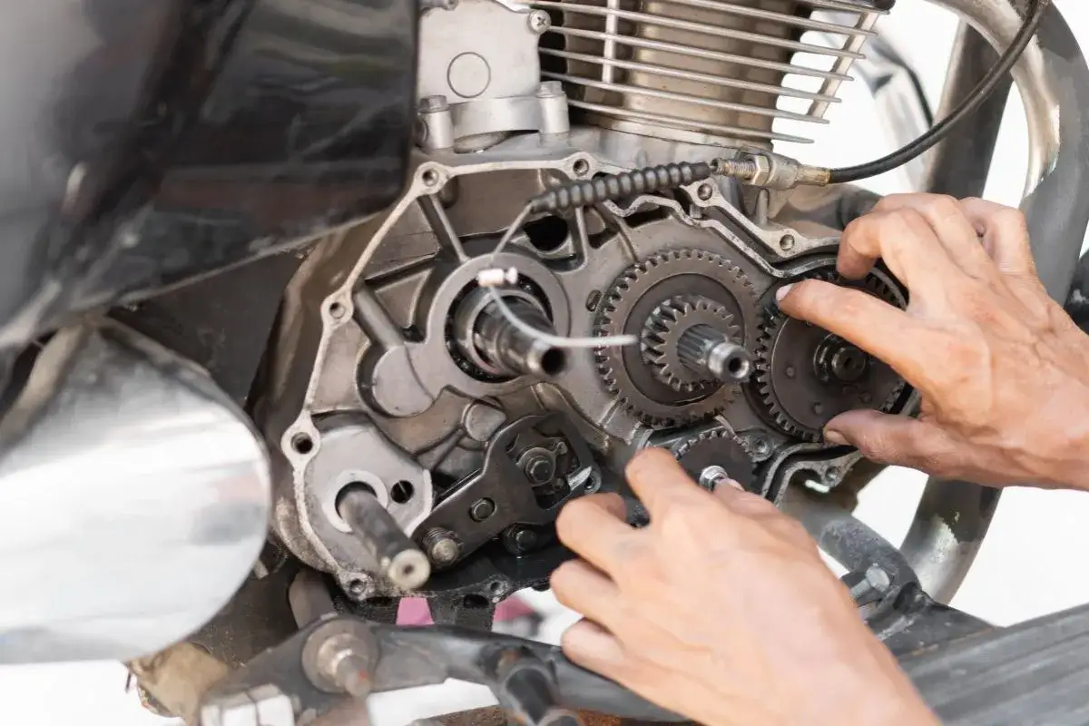 Mani che lavorano sul motore di una moto, ingranaggi visibili. Potrebbe essere legato alle cause di perdita potenza motore diesel.