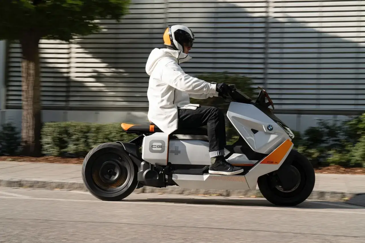 Mężczyzna w białej kurtce i kasku jedzie na futurystycznym skuterze BMW CE04.