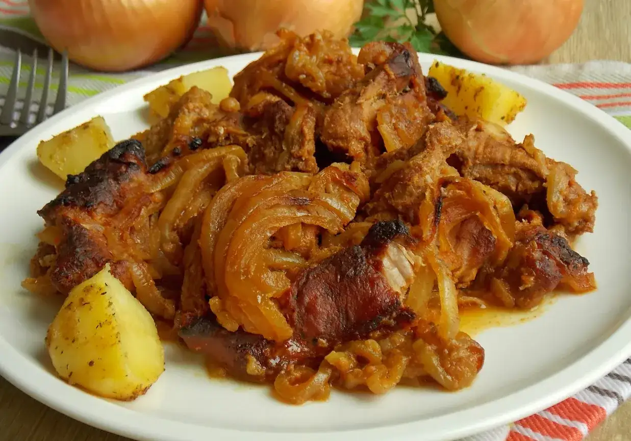 Karkówka pieczona w plastrach z cebulą, podana z ziemniakami. Aromatyczne danie, które rozpływa się w ustach.