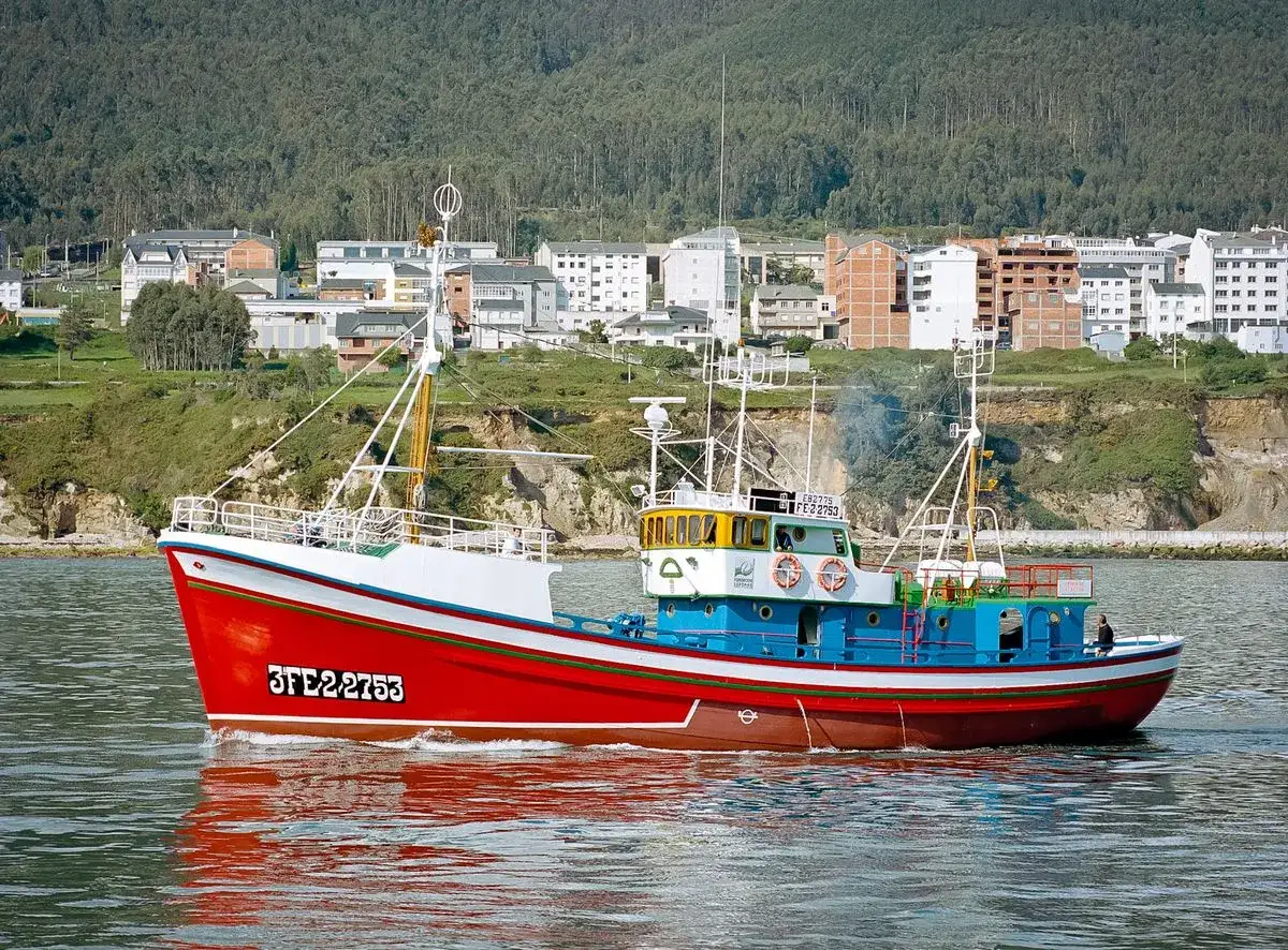 El barco museo boniteiro Reina del Carmen navega con su casco rojo y azul, reflej&aacute;ndose en el agua.