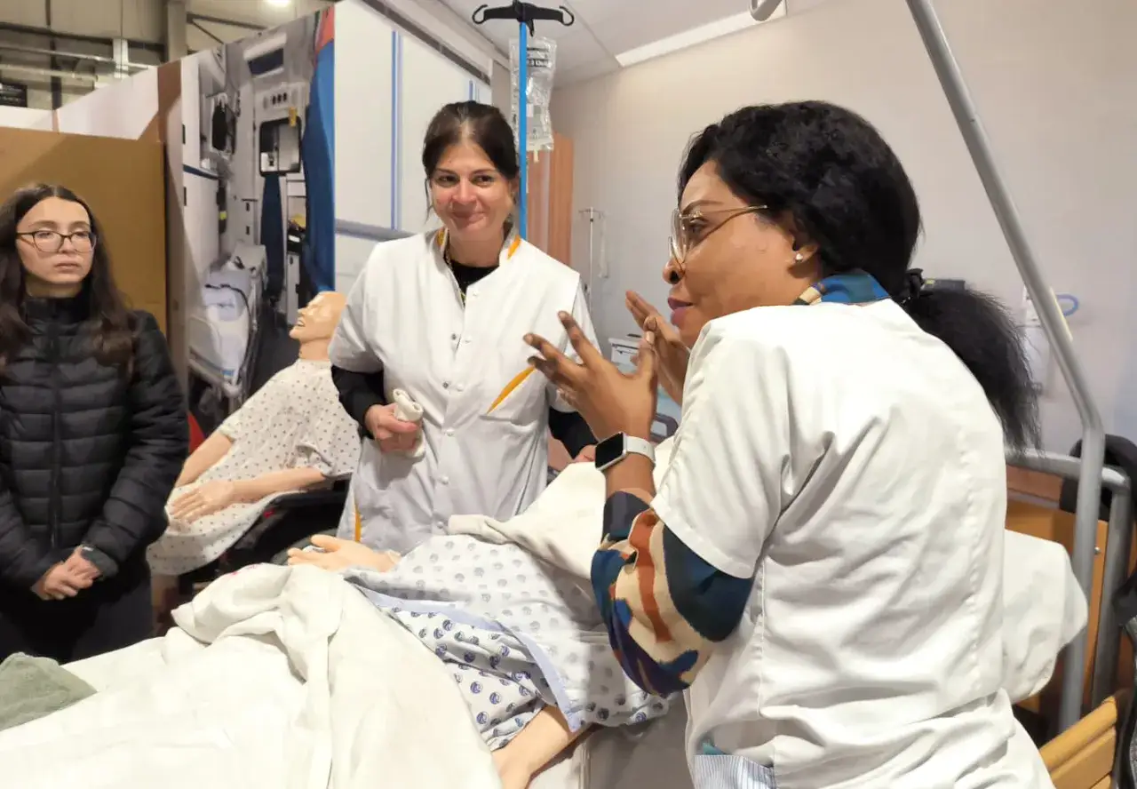 Une aide soignante belge, en formation, explique une proc&eacute;dure &agrave; des mannequins dans une salle de simulation m&eacute;dicale.