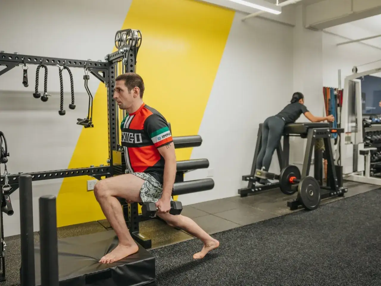 Mann macht Ausfallschritte mit Hantel, Frau trainiert R&uuml;cken. Verschiedene Kraft Arten im Fitnessstudio.