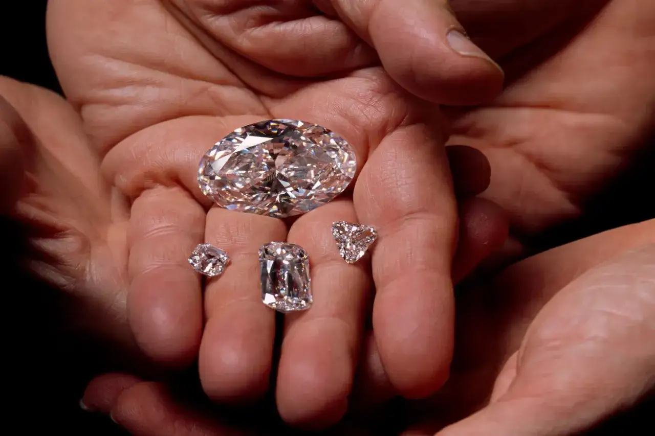Mani che stringono diversi diamanti, uno grande ovale e quattro più piccoli di varie forme. Il loro scintillio evoca il diamante significato di eternità e purezza.