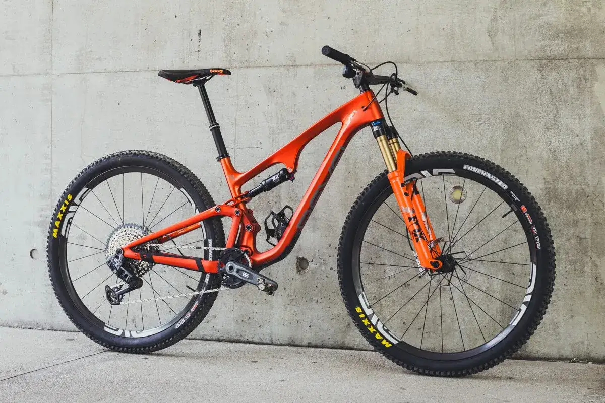 Orange full-suspension mountain bike, ready for a revel ranger v2 review. Features Maxxis tires and Fox suspension.