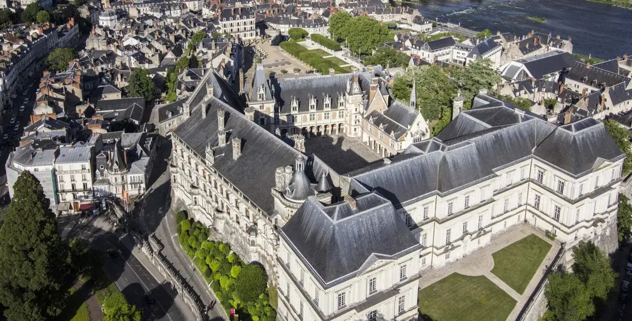 Vue a&eacute;rienne du **ch&acirc;teau de Blois**, un ensemble architectural majestueux avec ses toits d'ardoise et ses fa&ccedil;ades imposantes, dominant la ville et la Loire.
