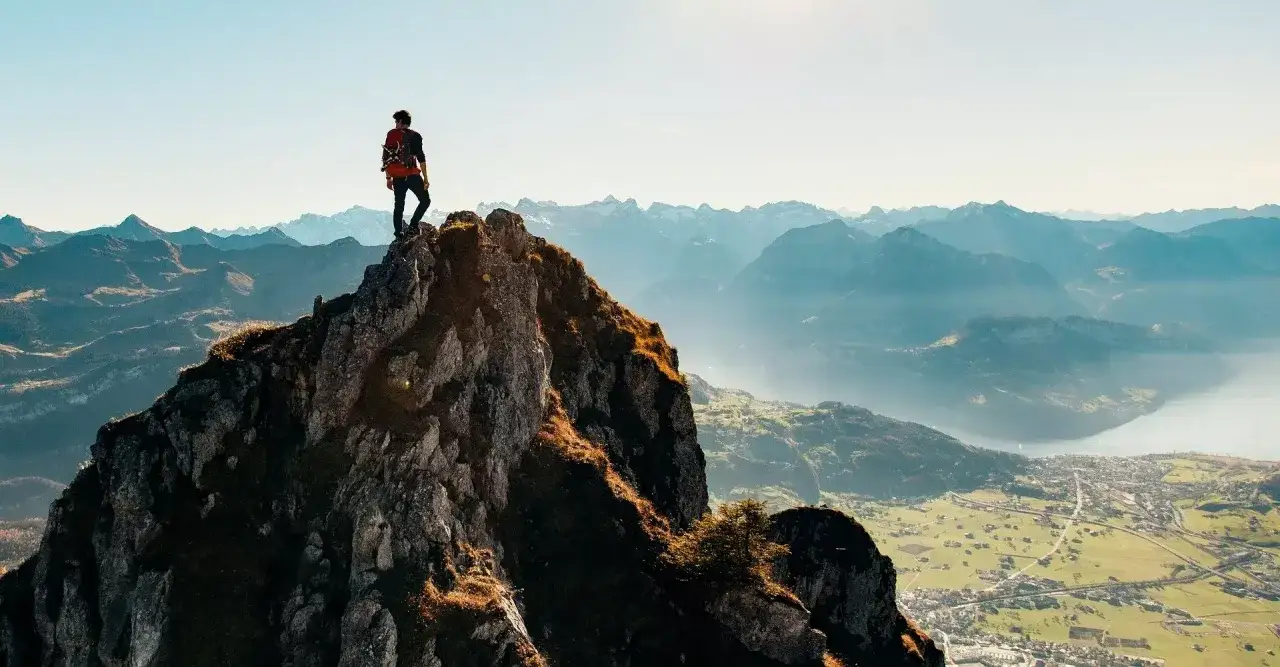 Alpinista na szczycie g&oacute;ry, podziwiający panoramę. Pokonanie trudności i zdobycie celu to często najtrudniejsze momenty.