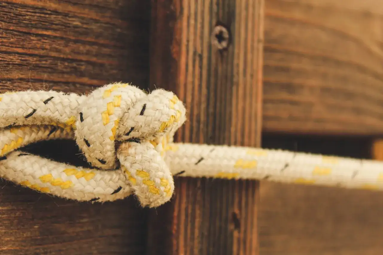 Un nudo firme en paracord, una cuerda resistente y vers&aacute;til, sujeta madera r&uacute;stica.
