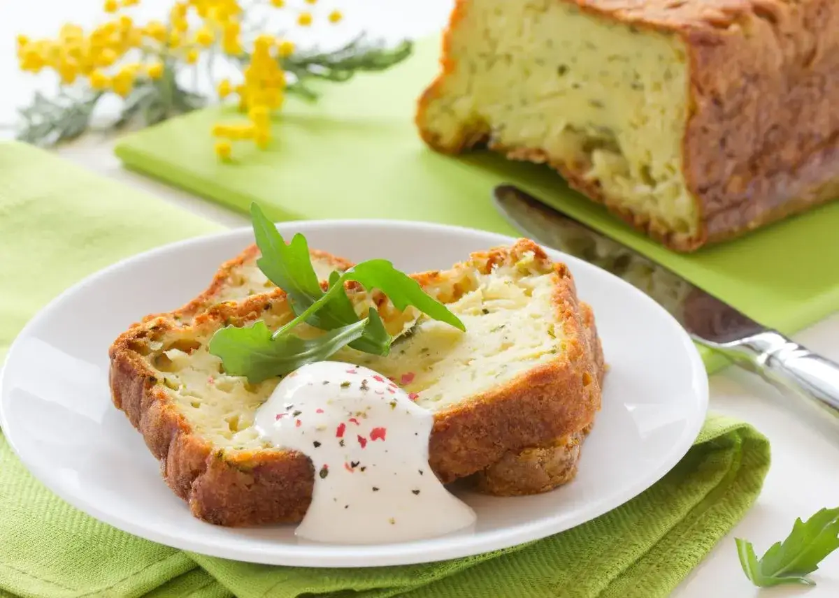 Rebanadas de pastel de calabac&iacute;n con salsa cremosa y r&uacute;cula, decoradas con flores amarillas.