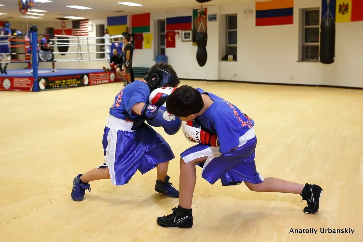 Two young boxers in blue shorts and shirts spar in a gym, practicing soviet style boxing.