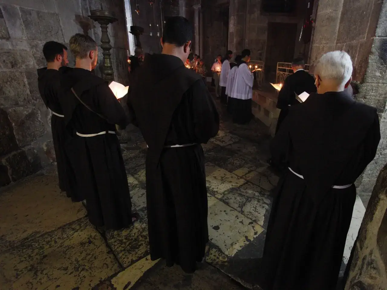 M&ouml;nche in schwarzen Kutten, die eine katholische Ordenliste studieren, stehen in einer Kirche.