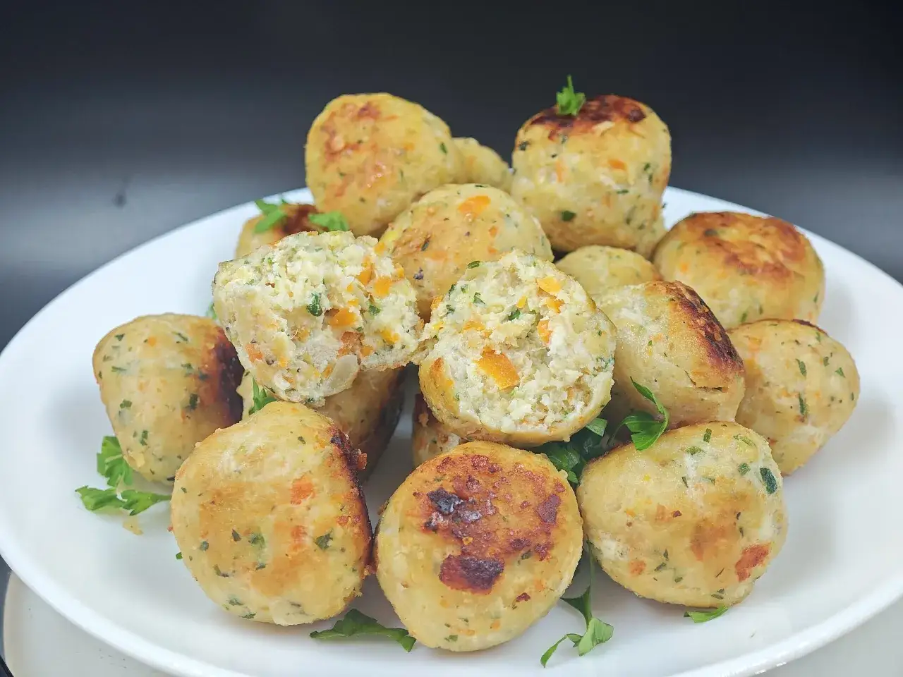 Polpette di pollo dorate e saporite, con pezzetti di carota e prezzemolo, servite su un piatto bianco.