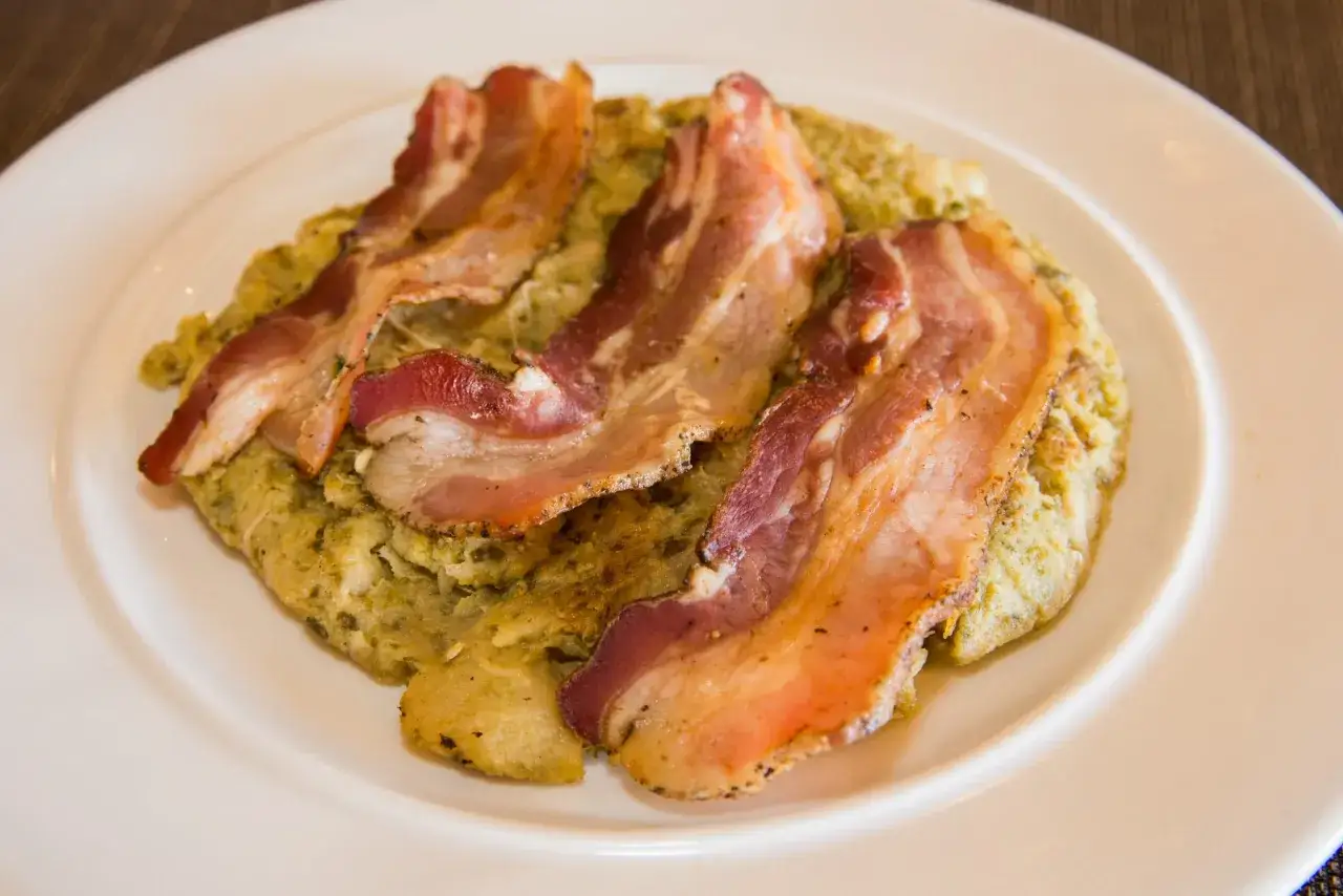 Trinxat de la Cerdanya, un plato tradicional con patata, col y tocino crujiente, servido en un plato blanco.