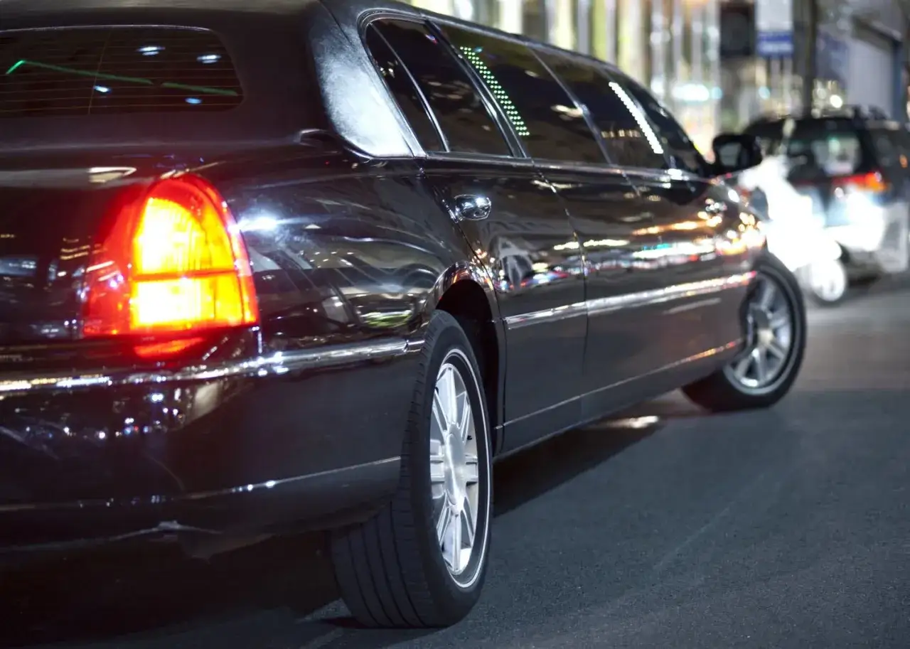 Czarna limuzyna, symbol luksusu i potencjalnych uber black zarobków. Błyszczące odbicia świateł miasta na karoserii.