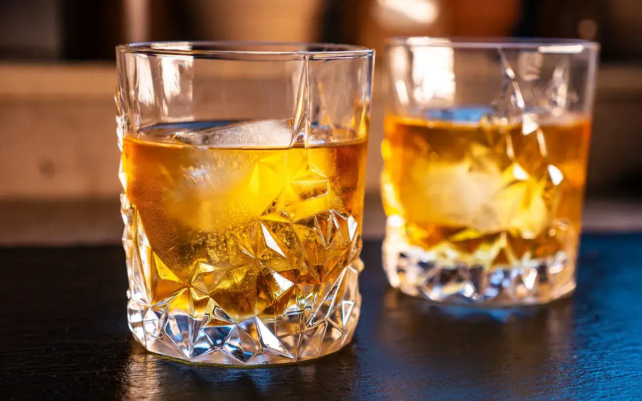 Zwei Gl&auml;ser mit bernsteinfarbenem Whisky, in denen man Whisky mit Eis trinkt. Das Licht bricht sich im geschliffenen Glas.