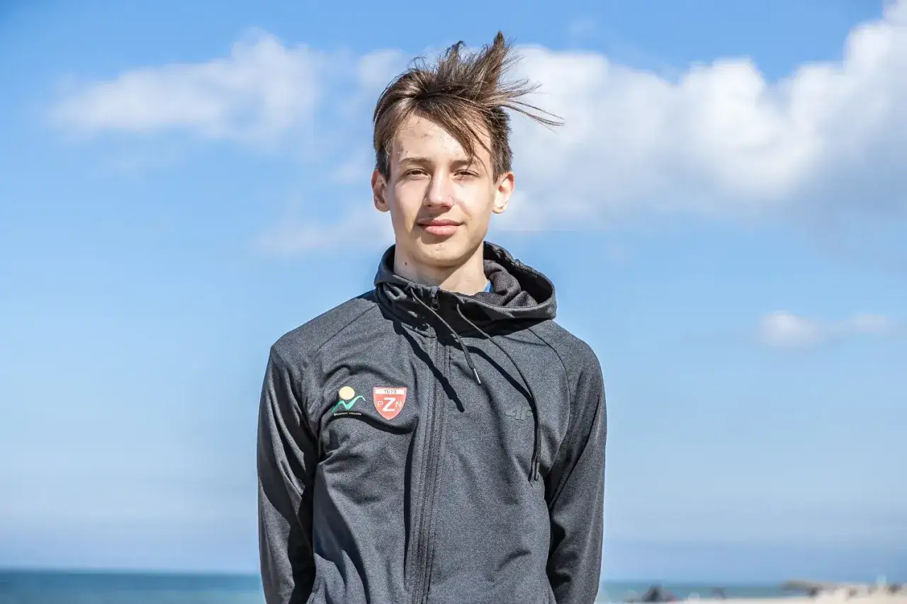 Kacper Tomasiak, młody sportowiec, na tle błękitnego nieba. Jego wzrost jest imponujący jak na jego wiek.
