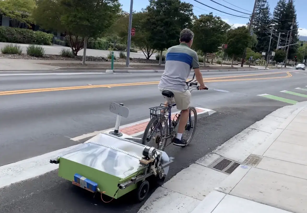 Mann fährt Fahrrad mit selbstgebauter Kehrmaschine.