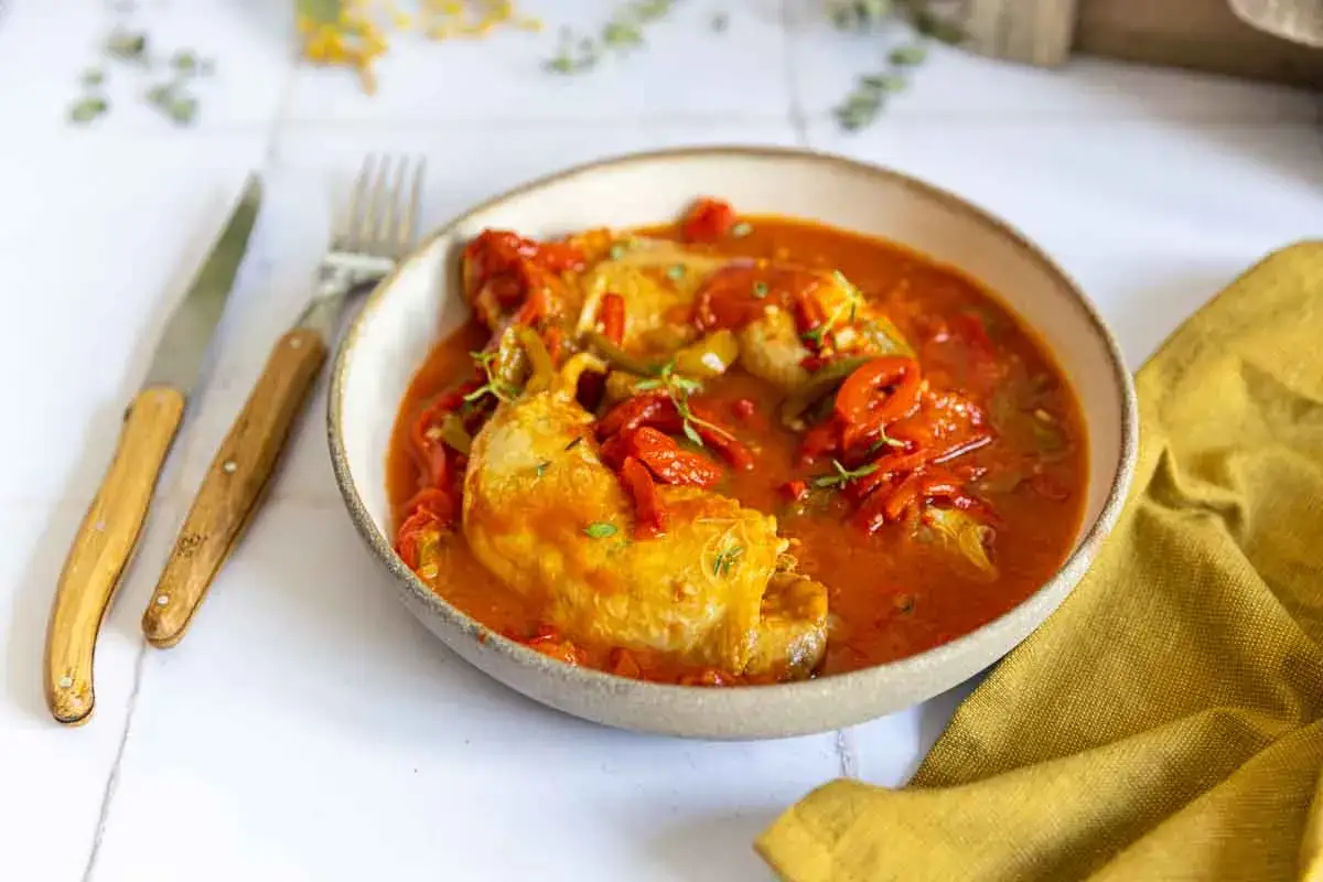 Un plat de poulet basquaise savoureux, pr&eacute;par&eacute; au Cookeo, servi dans un bol avec des poivrons rouges et verts.