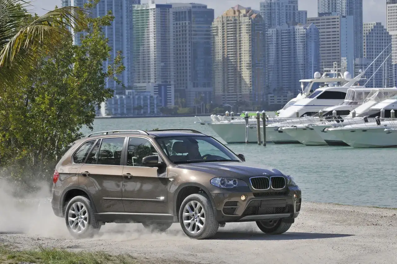 Brązowy BMW X5 na drodze szutrowej, w tle Miami i jachty. Wiele pozytywnych bmw x5 opinie potwierdza jego wszechstronność.