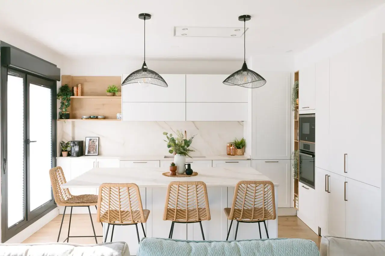 Cocinas modernas con isla central y sal&oacute;n integrado. Tres taburetes de mimbre rodean la isla, con l&aacute;mparas colgantes negras.
