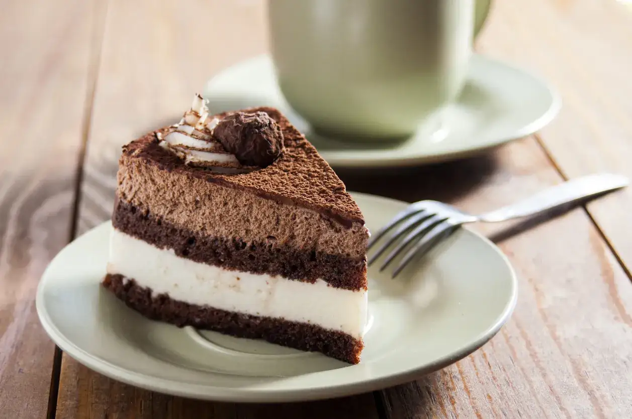 Pyszny tort kawowy z mascarpone, oprószony kakao, czeka na talerzyku obok filiżanki kawy.