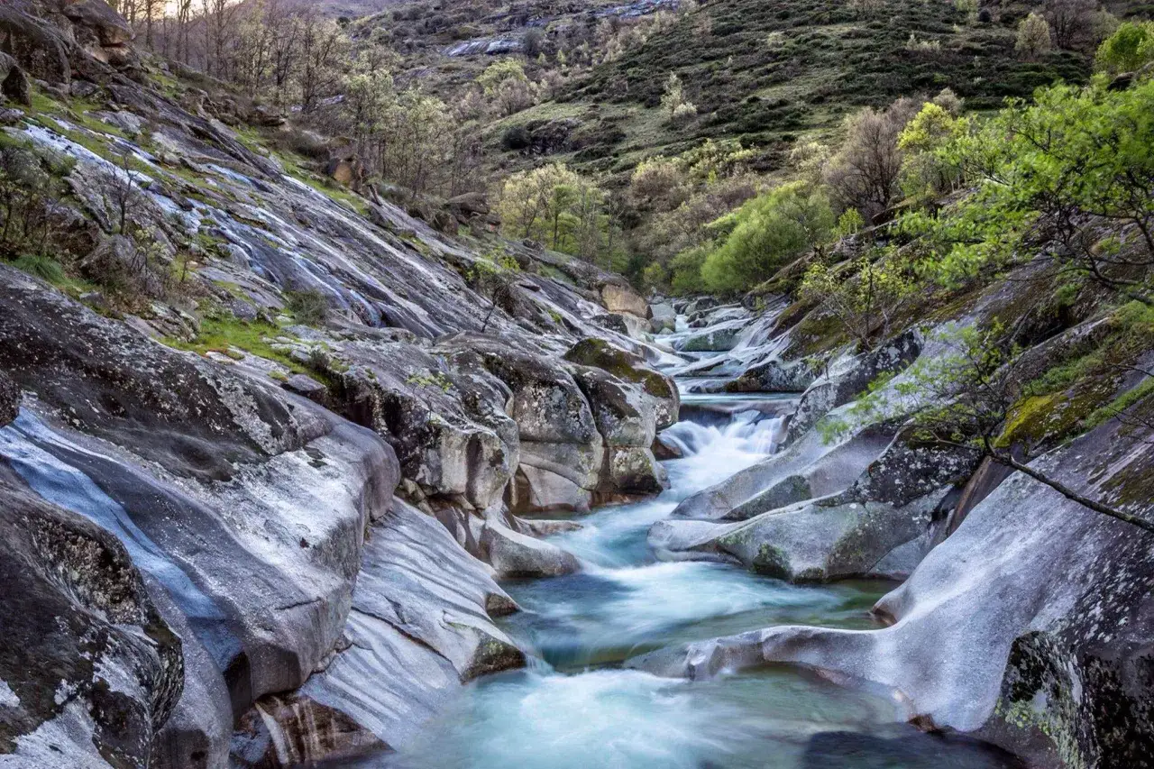 Un r&iacute;o de aguas cristalinas fluye entre rocas erosionadas, formando **los pilones** naturales en un paisaje monta&ntilde;oso cubierto de vegetaci&oacute;n.